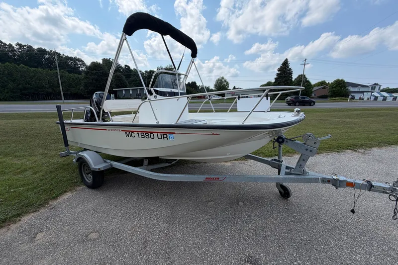 Slide: The Image of 2018 Boston Whaler 150 Montauk boat on trailer, parked on roadside under blue sky. - 1