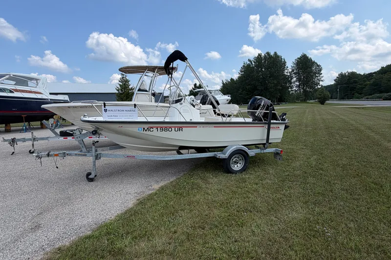 Slide: The Image of 2018 Boston Whaler 150 Montauk boat on trailer, parked on grass under blue sky. - 0