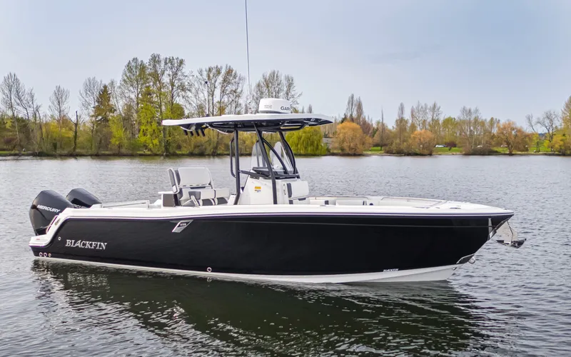 Slide: The Image of A sleek, black Blackfin 252 CC boat from 2027 on calm water, surrounded by trees. - 2