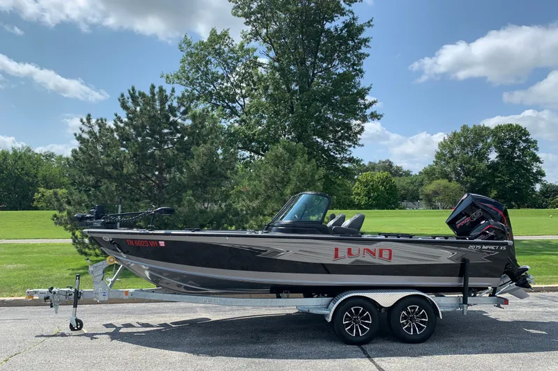 The Image of 2025 Lund 2075 Impact XS boat on trailer, parked outdoors under a clear sky. - 1