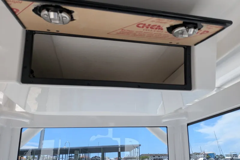 Slide: The Image of 2027 Caymas 26 HB boat interior storage compartment with open hatch and visible marina background. - 11