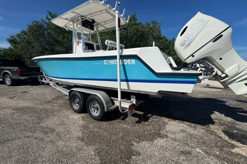 Slide: The Image of 2003 Contender 25 Open boat on trailer with Suzuki outboard motor, parked outdoors. - 3