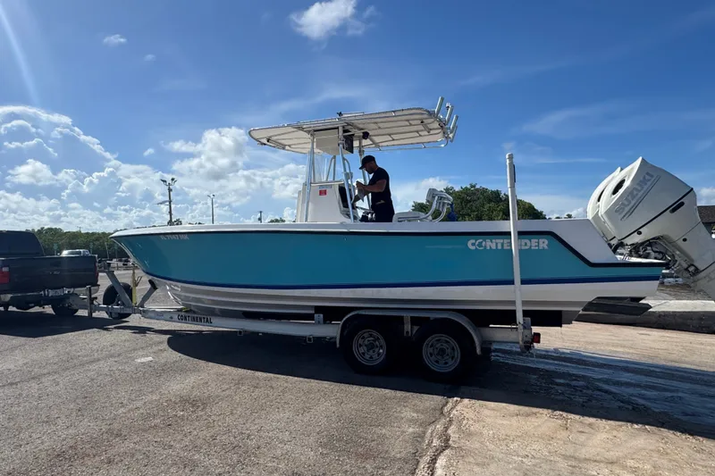 Slide: The Image of 2003 Contender 25 Open boat on trailer, blue hull, sunny day, person onboard. - 13