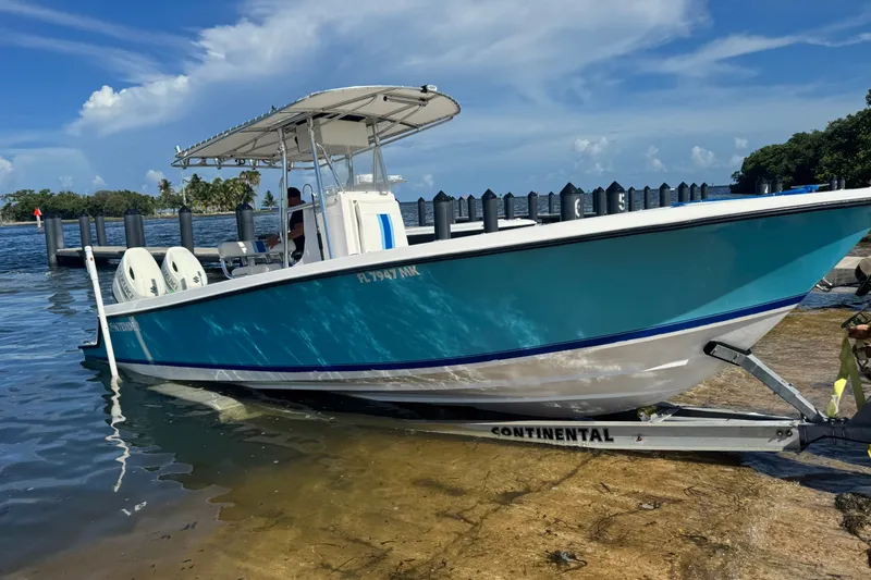 Slide: The Image of 2003 Contender 25 Open boat on trailer by the water, clear sky background. - 22