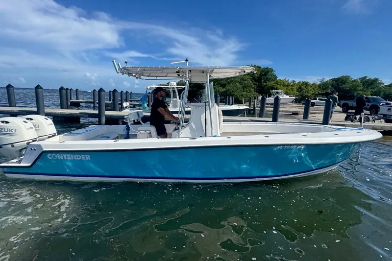 Slide: The Image of 2003 Contender 25 Open boat with blue hull, docked near a marina under a clear sky. - 25
