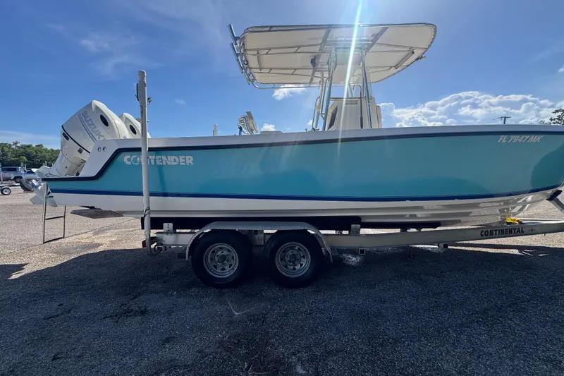 Slide: The Image of 2003 Contender 25 Open boat on trailer, blue hull, dual outboard engines, sunny day. - 9