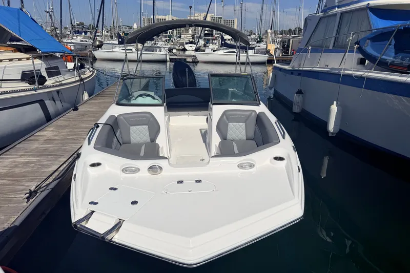 Slide: The Image of A modern NauticStar 203 DC Deck boat docked in a marina. It features a white exterior and gray seating. - 13