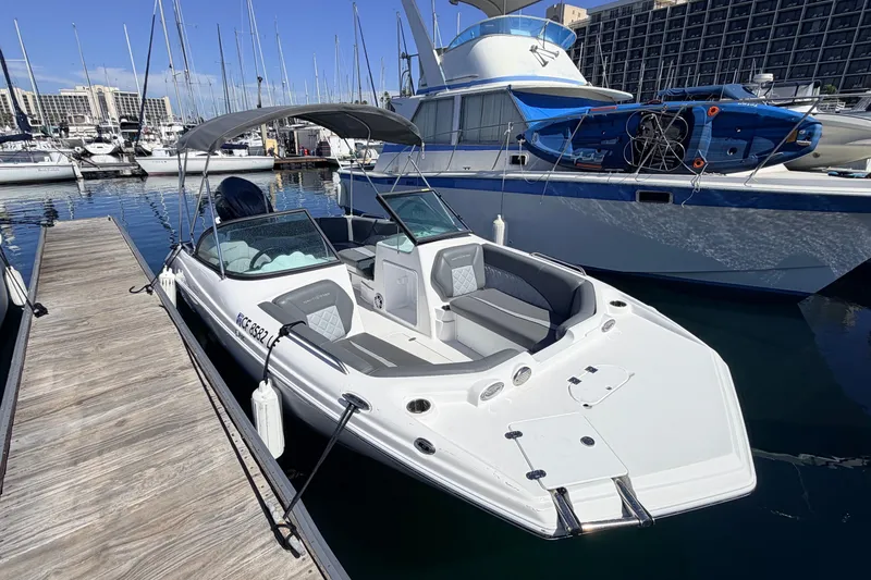 Slide: The Image of 2026 NauticStar 203 DC Deck boat docked at a marina, featuring sleek design and spacious seating. - 2