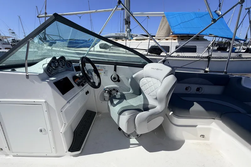 Slide: The Image of 2026 NauticStar 203 DC Deck boat interior with steering wheel and seating, docked at marina. - 10