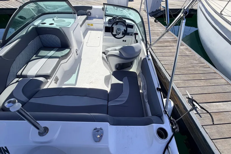 Slide: The Image of 2026 NauticStar 203 DC Deck boat interior with seating and steering wheel at dock. - 6