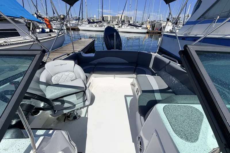 Slide: The Image of 2026 NauticStar 203 DC Deck boat interior at marina, featuring seating and steering wheel. - 8