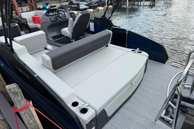 Slide: The Image of 2027 Harris Sunliner 210 pontoon boat interior with seating and steering console by the water. - 3