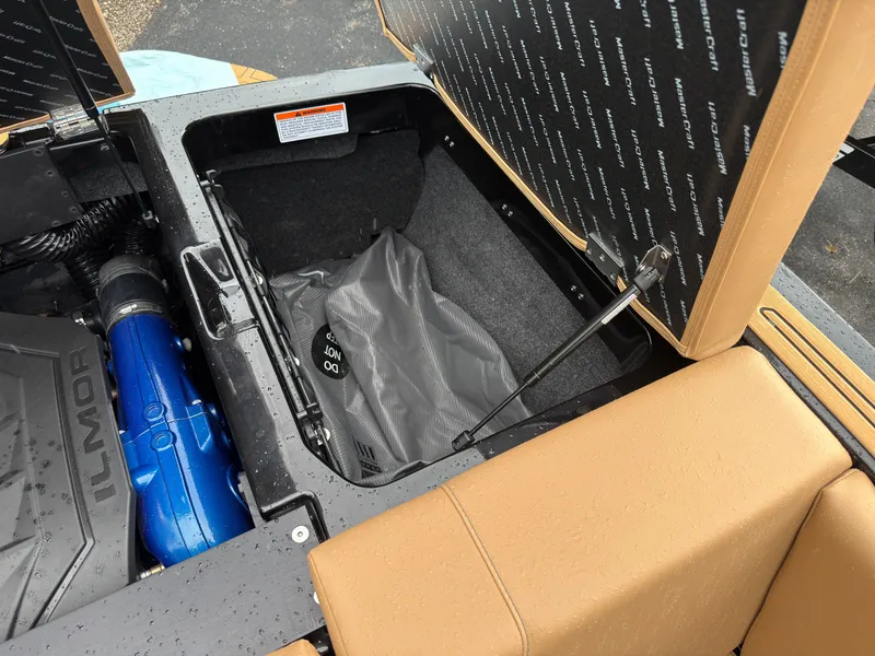 Slide: The Image of An open storage compartment in the rear of a 2027 MasterCraft NXT23 boat, featuring a blue Ilmor engine. - 14