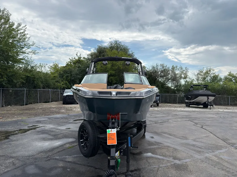 Slide: The Image of A 2027 MasterCraft NXT23 boat on a trailer in a parking area, surrounded by trees. - 3