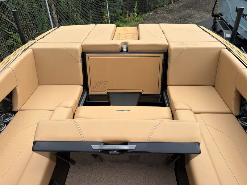Slide: The Image of The image shows the rear of a MasterCraft NXT23 boat with beige upholstery and a central storage area. - 23