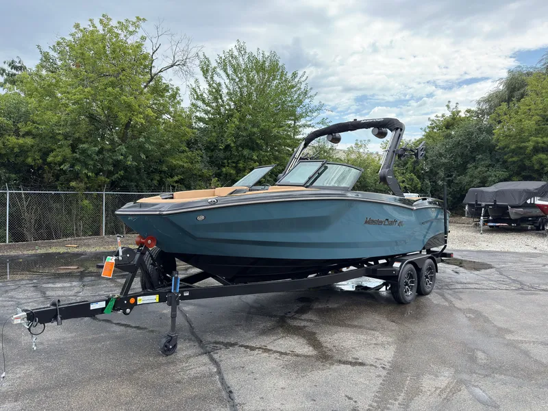 Slide: The Image of A 2027 MasterCraft NXT23 boat on a trailer in an outdoor setting. - 2