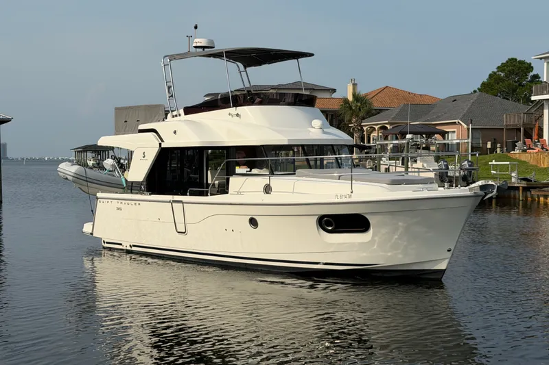 The Image of 2025 Beneteau Swift Trawler 35 cruising on a calm waterfront near residential docks. - 1