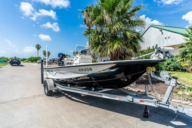 The Image of A 2018 Blue Wave 1900STL boat on a trailer, surrounded by palm trees and a building. - 1