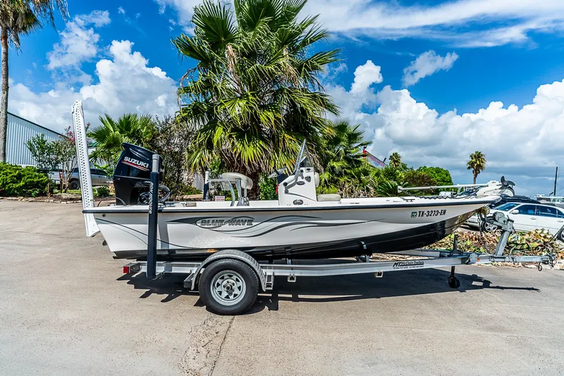 Slide: The Image of A 2018 Blue Wave 1900STL boat on a trailer, surrounded by palm trees and clear skies. - 2
