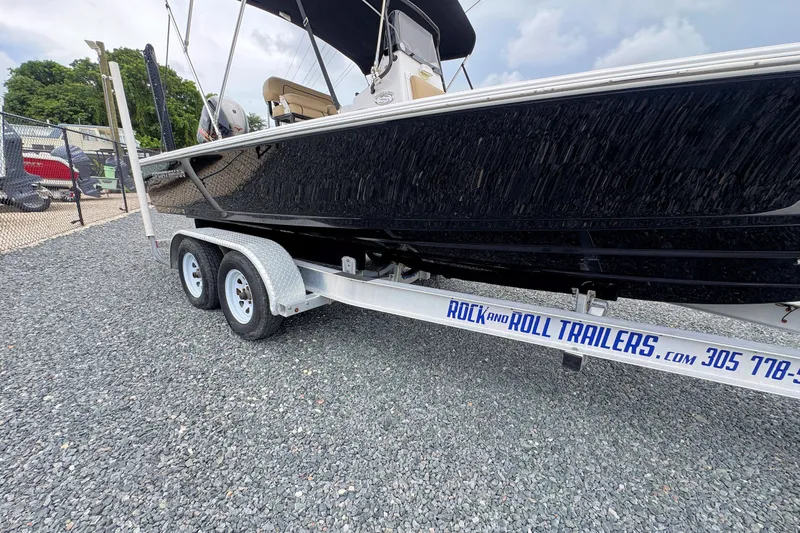 Slide: The Image of 2019 Sportsman Tournament 214 SBX Bay Boat on Rock and Roll trailer, parked on gravel. - 7