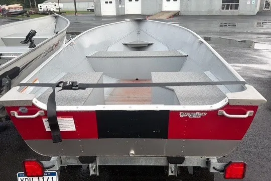 Slide: The Image of 2025 Lund WC-12 aluminum boat, red and silver, parked on a wet surface. - 12