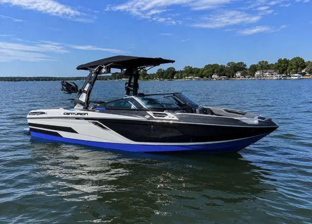 The Image of A 2023 Centurion Ri245 on a calm lake, featuring a blue and black hull. - 1