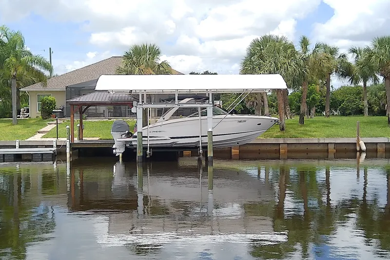 Slide: The Image of 2019 Regal 29 OBX boat docked under a canopy, surrounded by lush greenery and calm water. - 2