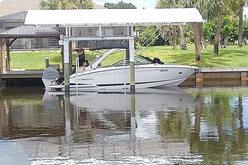 Slide: The Image of 2019 Regal 29 OBX boat docked under a canopy near a grassy shoreline. - 3