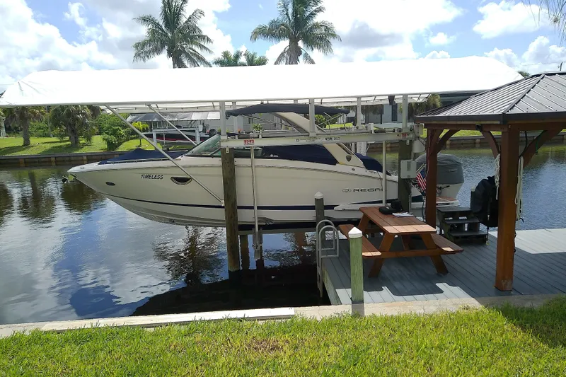 Slide: The Image of 2019 Regal 29 OBX boat docked on a lift by a canal with palm trees. - 4