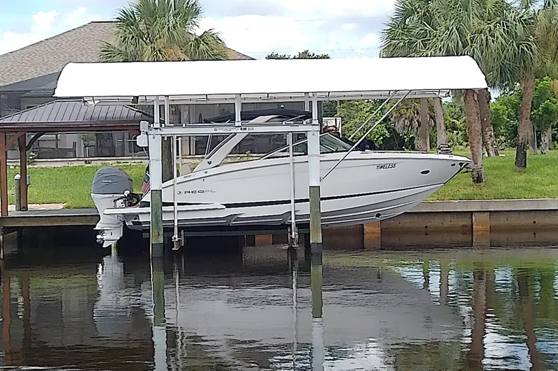 Slide: The Image of 2019 Regal 29 OBX boat docked on a lift by a waterfront property with palm trees. - 1