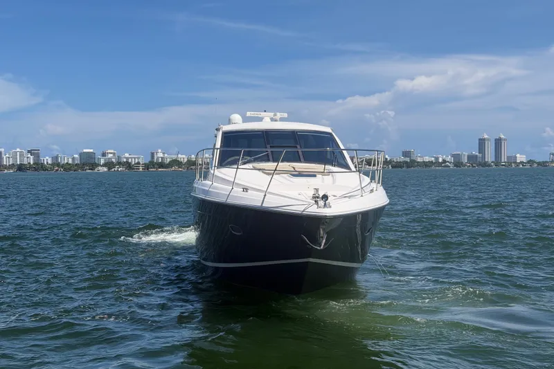 Slide: The Image of 2013 Regal 52 Sport Coupe yacht cruising on open water with city skyline backdrop. - 3