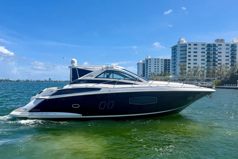 The Image of 2013 Regal 52 Sport Coupe yacht cruising near waterfront buildings under clear blue sky. - 1
