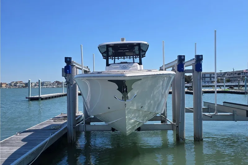 The Image of 2024 Fountain 32 NX boat docked on a lift in a marina under clear blue skies. - 4