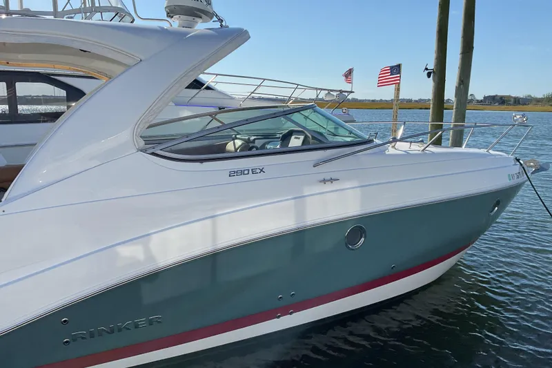 Slide: The Image of 2019 Rinker 290 Express Cruiser docked by the water with flags in the background. - 1