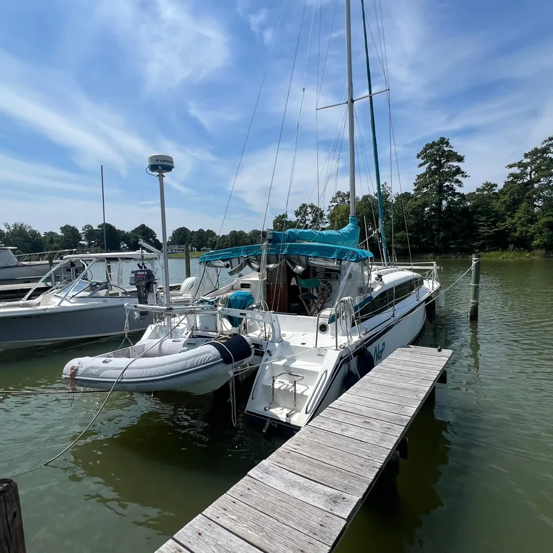 Slide: The Image of A 1993 Gemini Catamaran 3400 docked at a wooden pier. A dinghy is attached at the stern. - 3