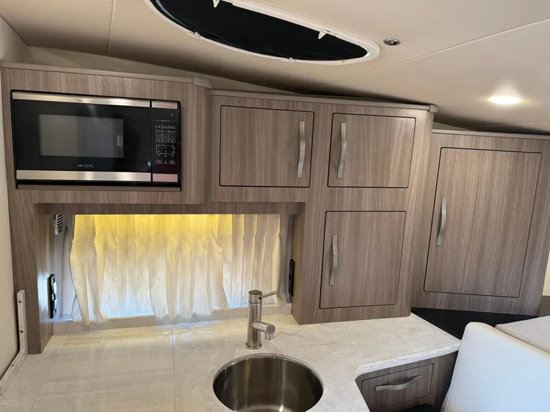 Slide: The Image of 2021 Regal 33 XO boat interior kitchen with microwave, sink, and wooden cabinets. - 19
