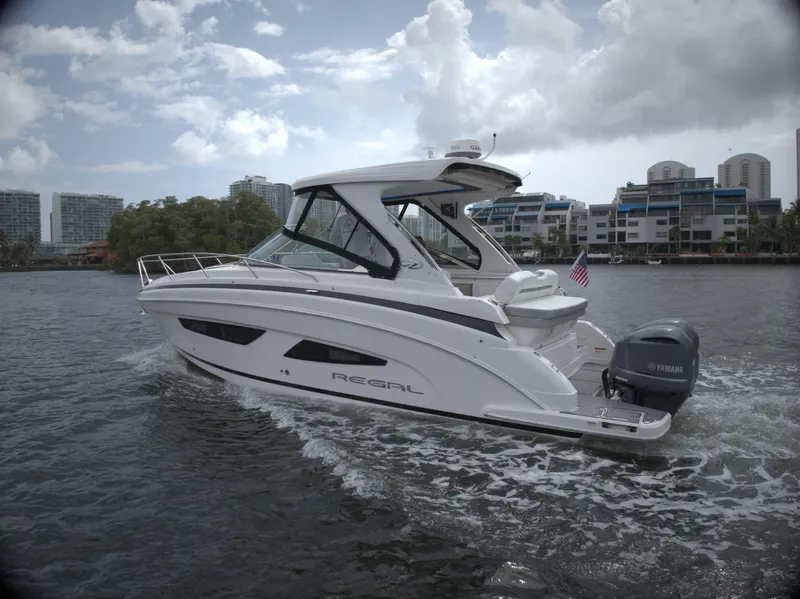 The Image of 2021 Regal 33 XO boat cruising on water with cityscape background. - 1