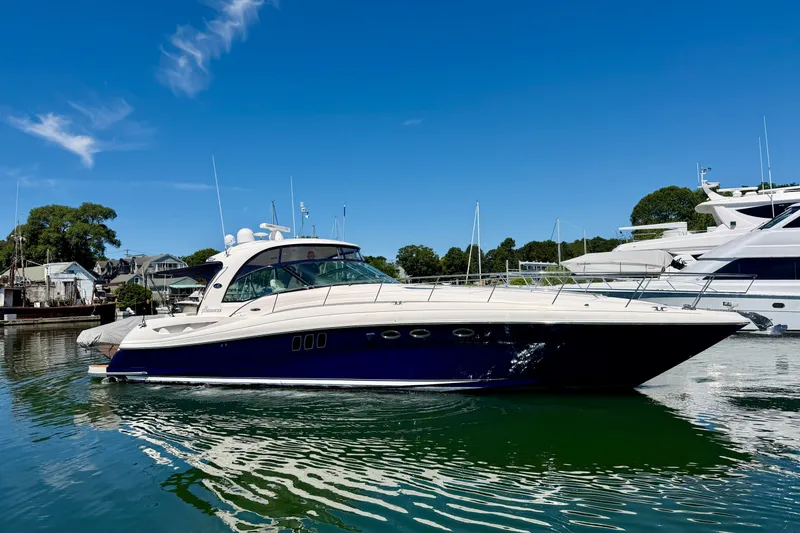 The Image of 2006 Sea Ray 52 Sundancer yacht docked in a serene marina under a clear blue sky. - 0