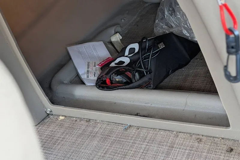 Slide: The Image of Storage compartment in a 2021 Sun Tracker Bass Buggy 16 XL with cables and documents. - 25