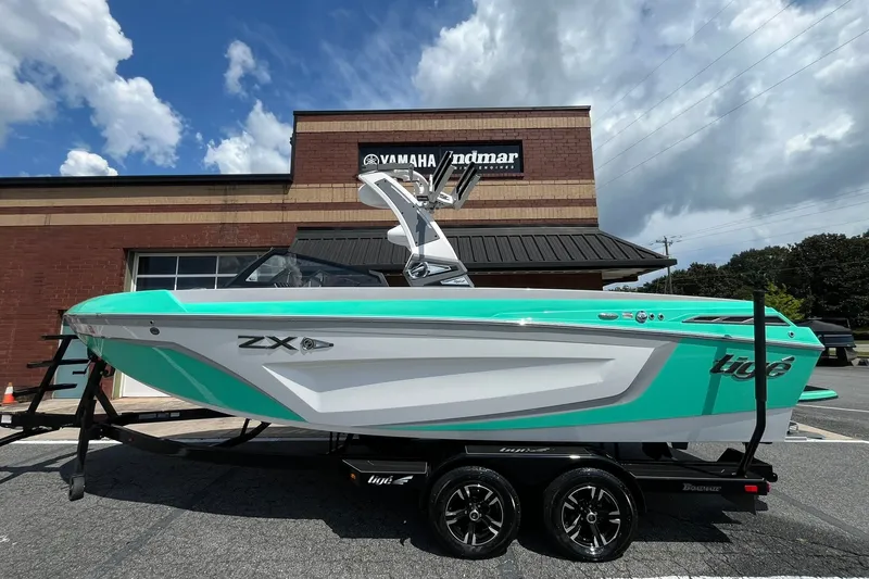 Slide: The Image of 2020 Tigé 23ZX boat in turquoise and white, parked outside a Yamaha dealership. - 1