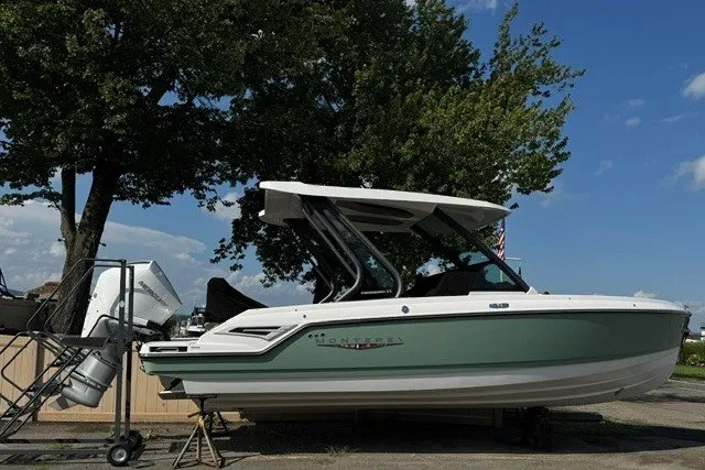 The Image of 2027 Monterey Elite 25 OB boat, green and white, parked outdoors under a clear blue sky. - 0