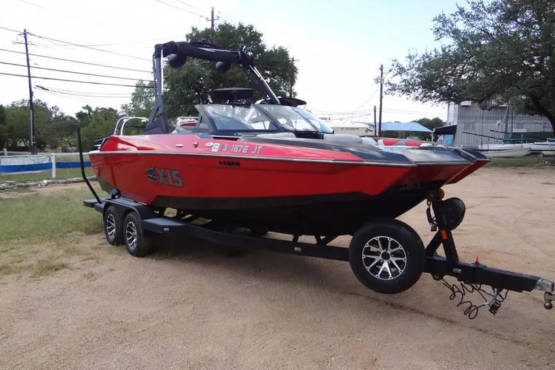 The Image of Red 2020 Axis A22 boat on trailer, parked outdoors with trees and buildings in background. - 0