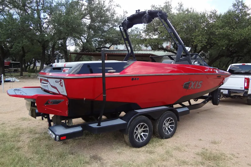 Slide: The Image of Red 2020 Axis A22 boat on trailer, parked outdoors near trees. - 2