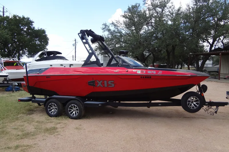 Slide: The Image of Red 2020 Axis A22 boat on trailer, parked outdoors with trees in background. - 1
