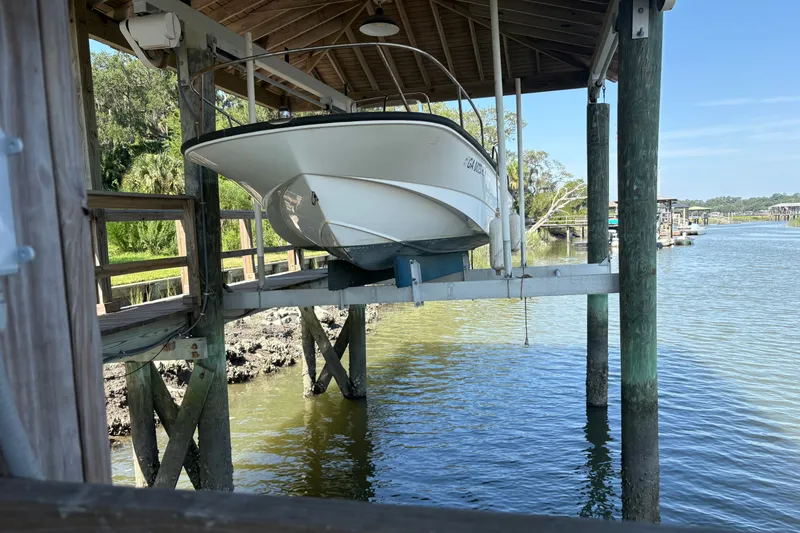 The Image of 2014 Boston Whaler 170 Montauk boat on a lift by a serene riverside dock. - 3