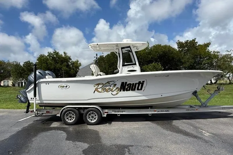 The Image of 2022 Sea Hunt Gamefish 27FS boat on trailer, labeled "Reely Nauti," under cloudy sky. - 30