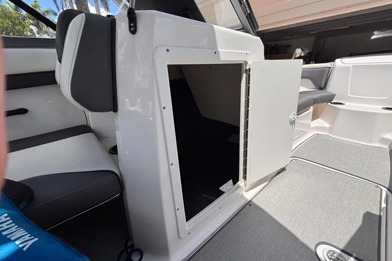 Slide: The Image of 2022 Yamaha AR210 boat interior storage compartment with open door, showcasing seating and flooring. - 42