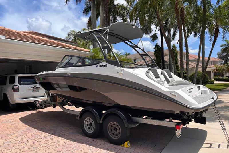 The Image of 2022 Yamaha Boats AR210 on trailer in sunny driveway with palm trees. - 0