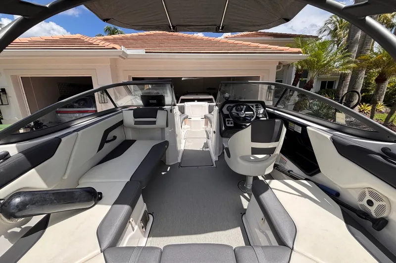 Slide: The Image of 2022 Yamaha Boats AR210 interior with sleek seating and modern dashboard, parked near a house. - 21