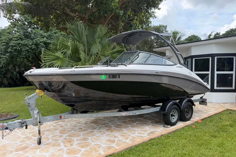 The Image of 2022 Yamaha AR210 boat on trailer, parked in a lush garden setting. - 0